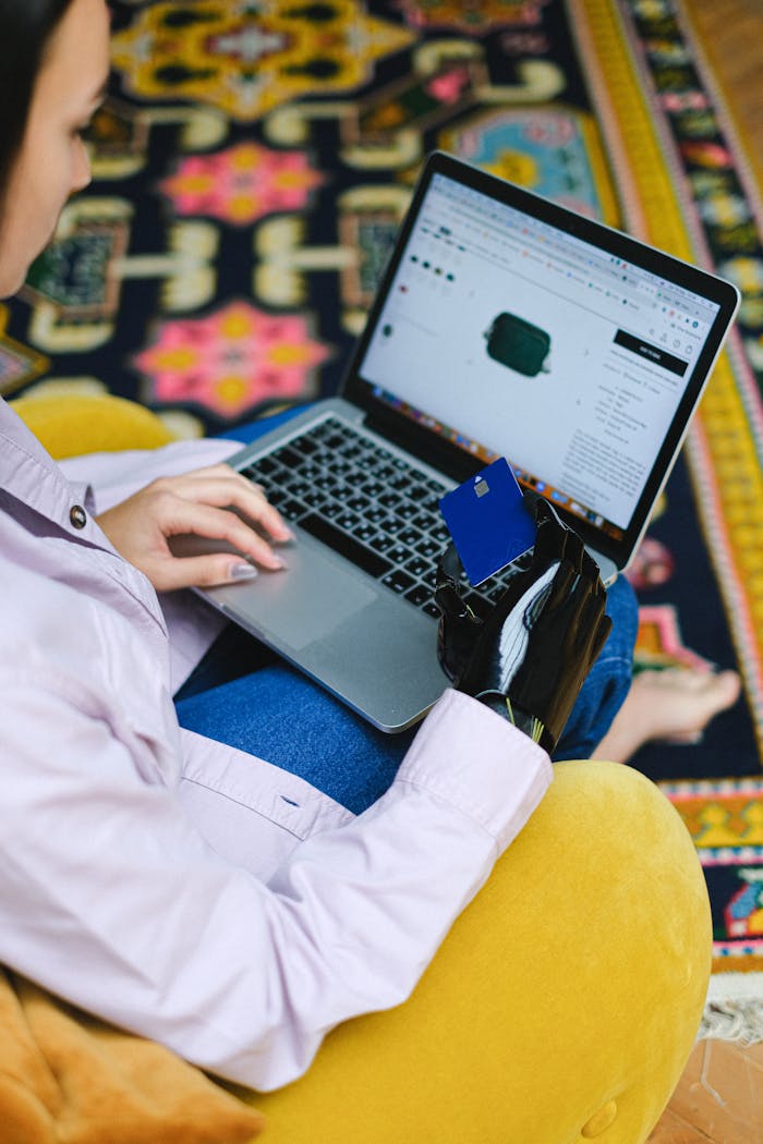 A person using a prosthetic arm shops online with a laptop and bank card indoors.